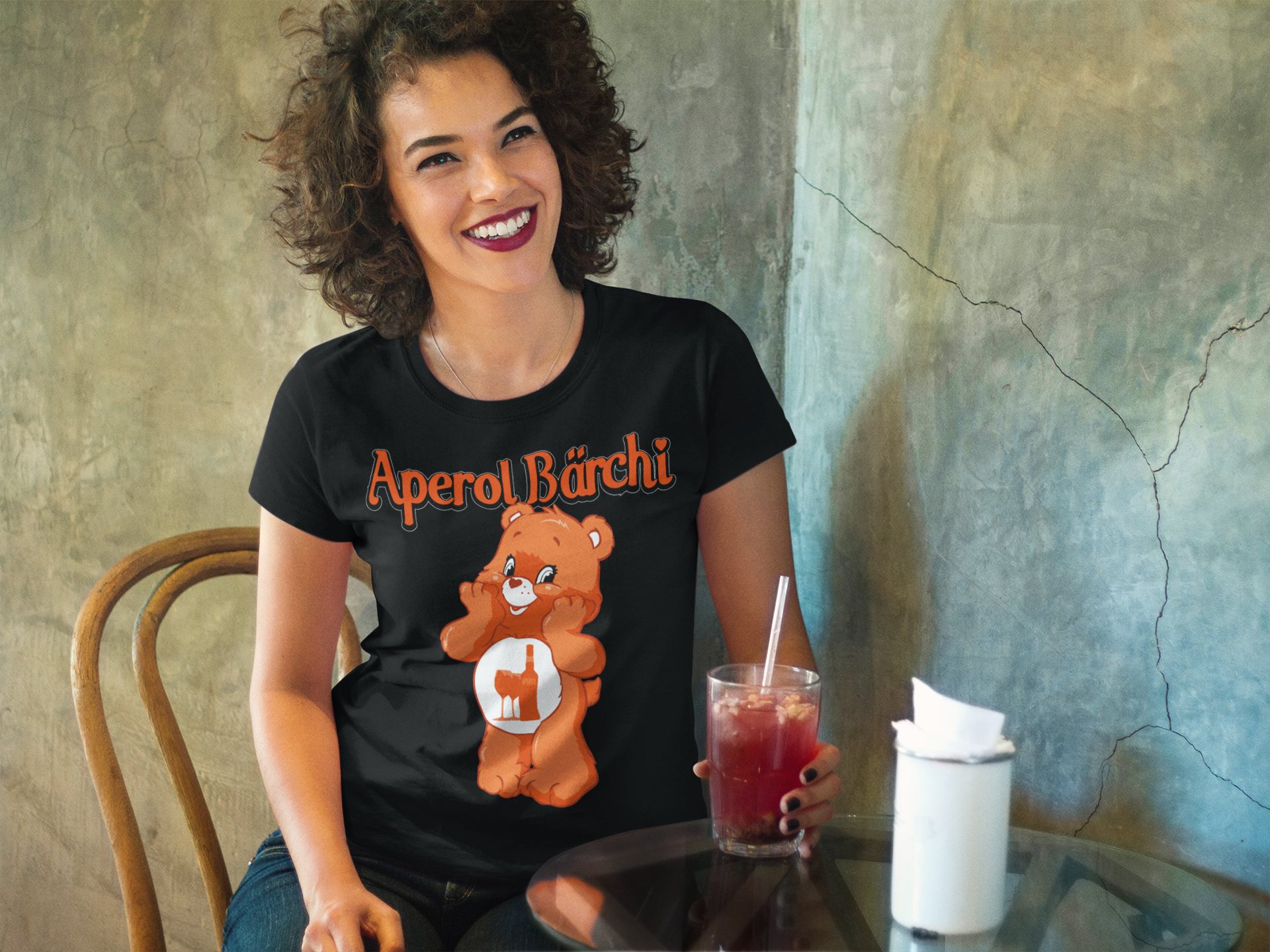 Dunkelhaarige Frau trägt Schwarzes Aperol Bärchi Damenshirt mit Flasche und Glas
