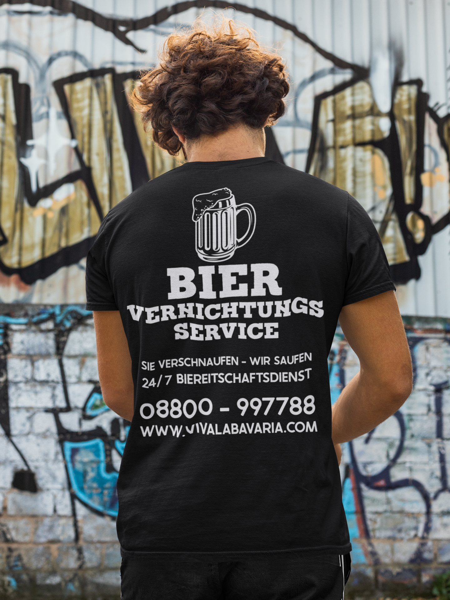 Mann steht vor einer Bemalten Wand und trägt ein Bier Vernichtungs Service T-Shirt