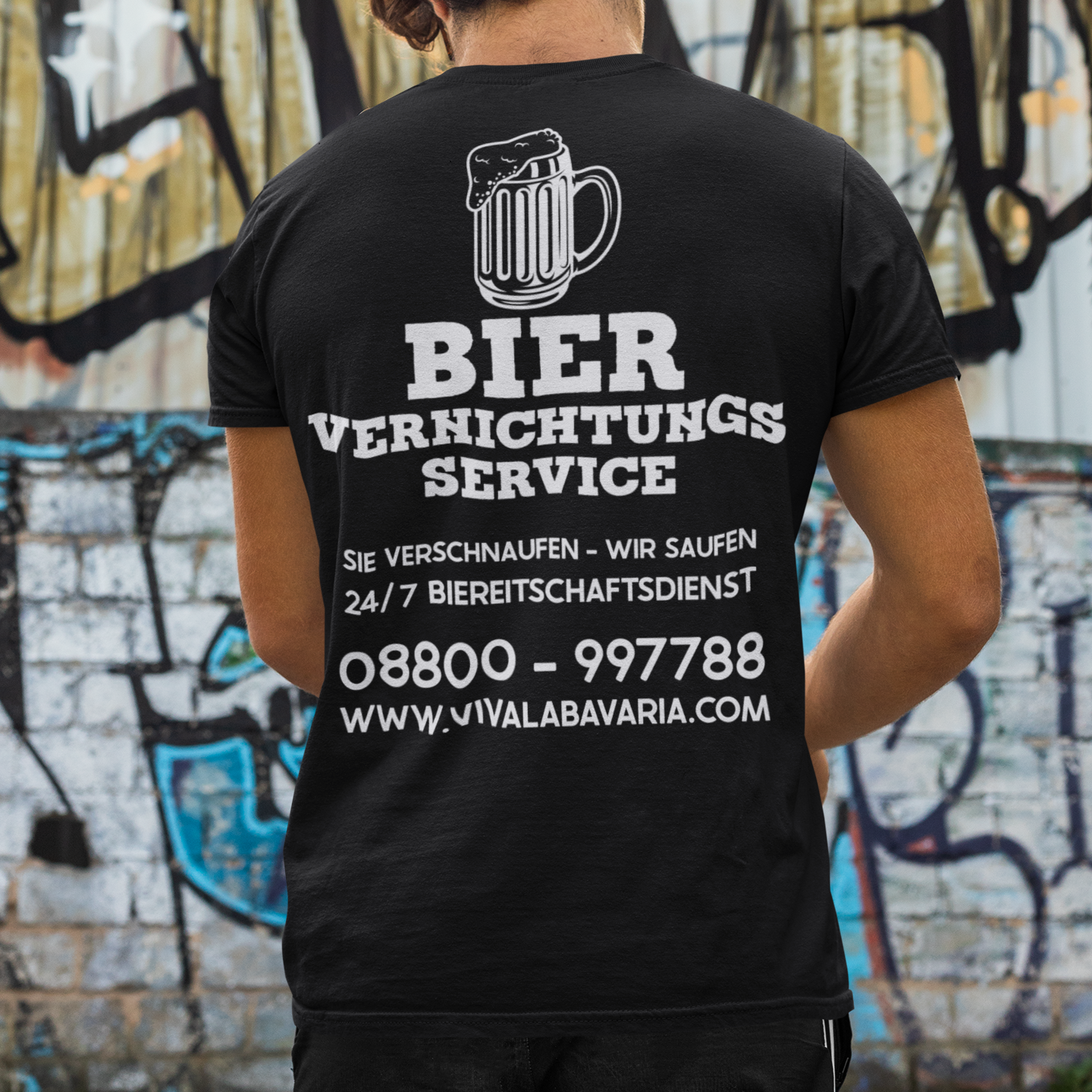 Mann steht vor einer Bemalten Wand und trägt ein Bier Vernichtungs Service T-Shirt