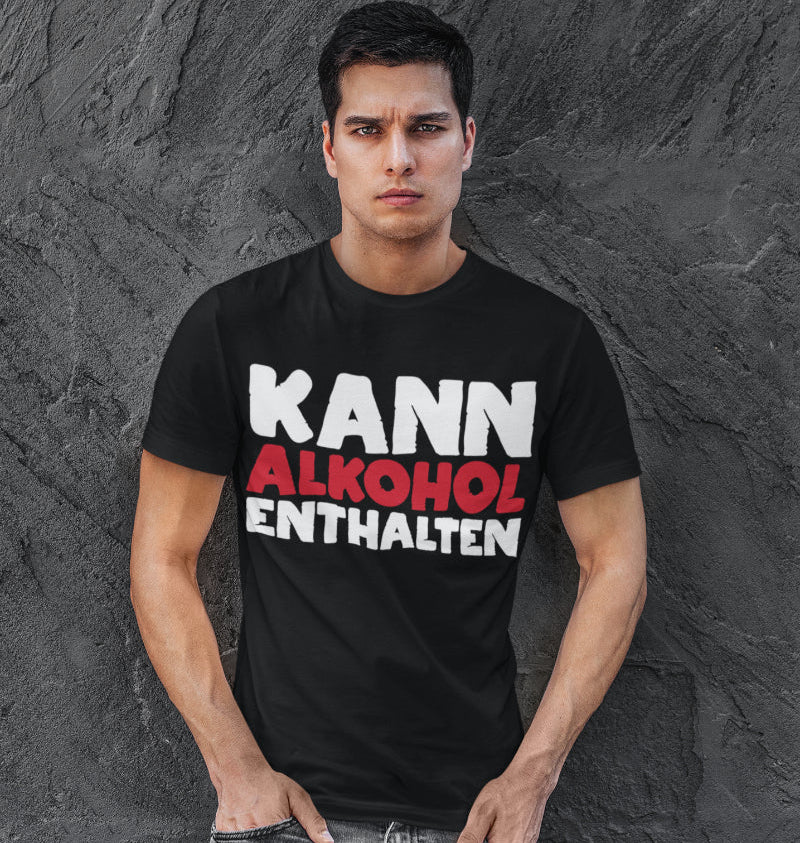 Ein Mann trägt ein Alkohol Spruch Shirt KANN ALKOHOL ENTHALTEN im Studio und posiert vor grauer Wand