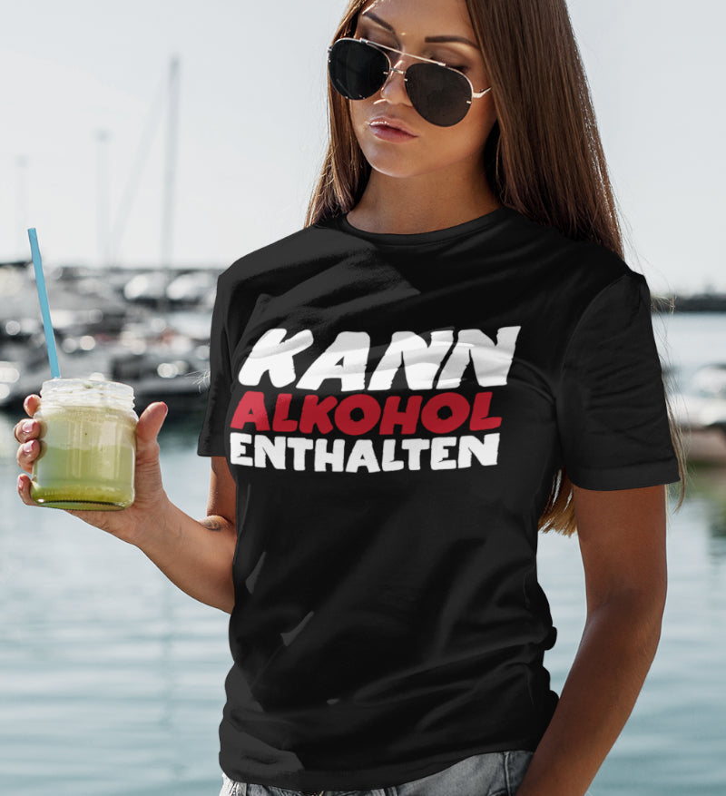 Eine Frau trägt das Kann Alkohol enthalten Shirt am Yachthafen und hält einen Cocktail