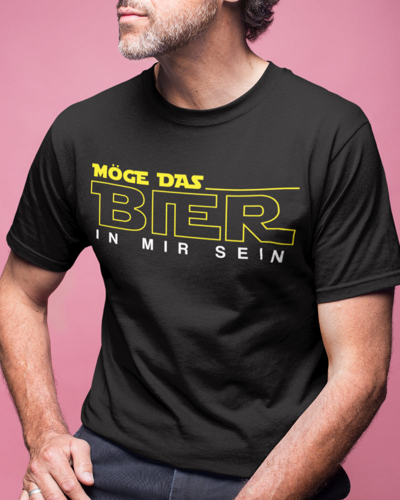 Ein Mann trägt das Möge das Bier in mir sein Shirt im Studio und sitzt auf einem Hocker