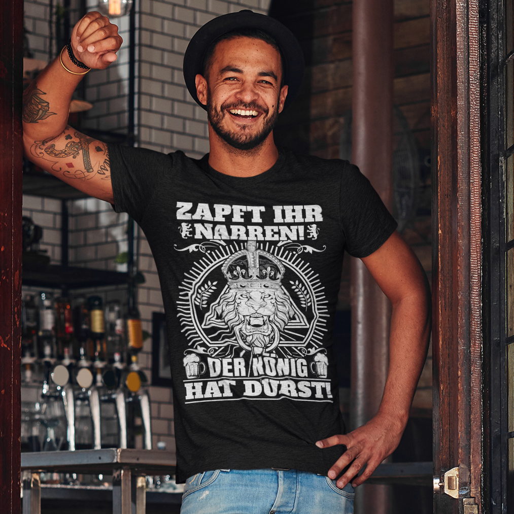 Ein Mann trägt das ZAPFT IHR NARREN Shirt an einem Bar Eingang und lehnt lässig am Geländer