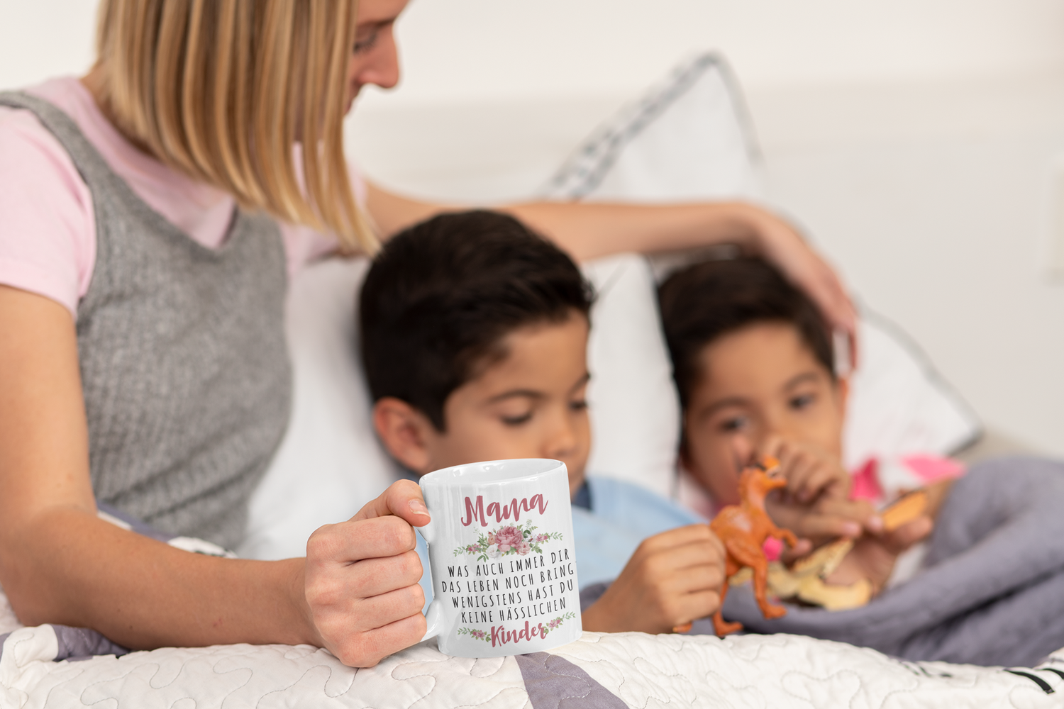 Mutter hält Muttertagstasse und liegt mit ihren Kindern im Bett